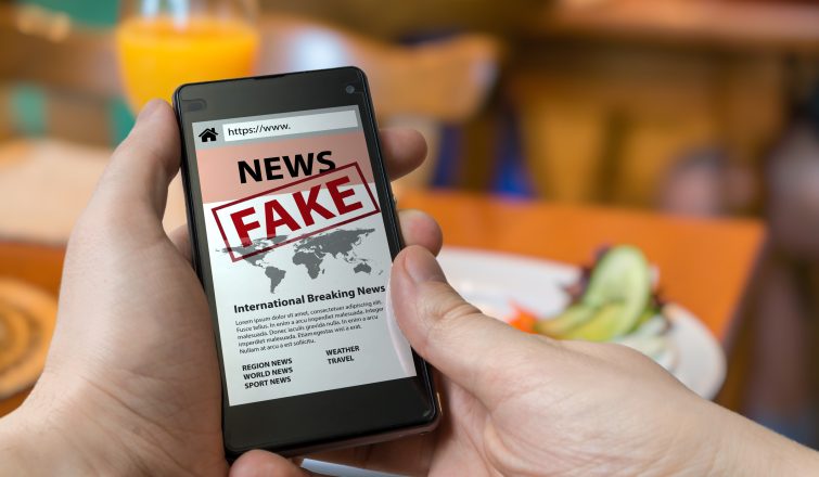 Man is holding smartphone and reading fake news on internet. Propaganda, disinformation and hoax concept.