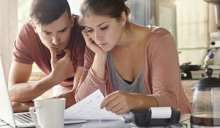 Young female and her unemployed husband with many debts doing paperwork together in kitchen, reading notification, informing that they must move out from their apartment because of non-payment